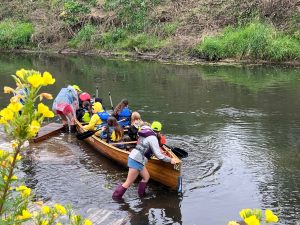 Students launch in a wooden canoe in a river